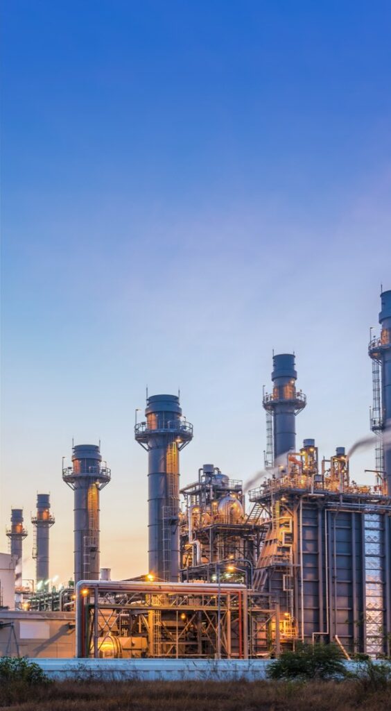 A photo of a refinery against a vibrant blue sky. Industrial foreground alit with warm lights.